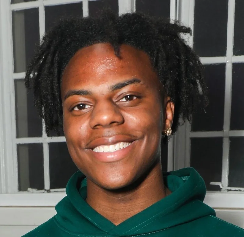 Le streamer iShowSpeed, de son vrai nom Darren Watkins Jr., en sweat vert devant une fen&ecirc;tre, souriant face &agrave; la cam&eacute;ra.