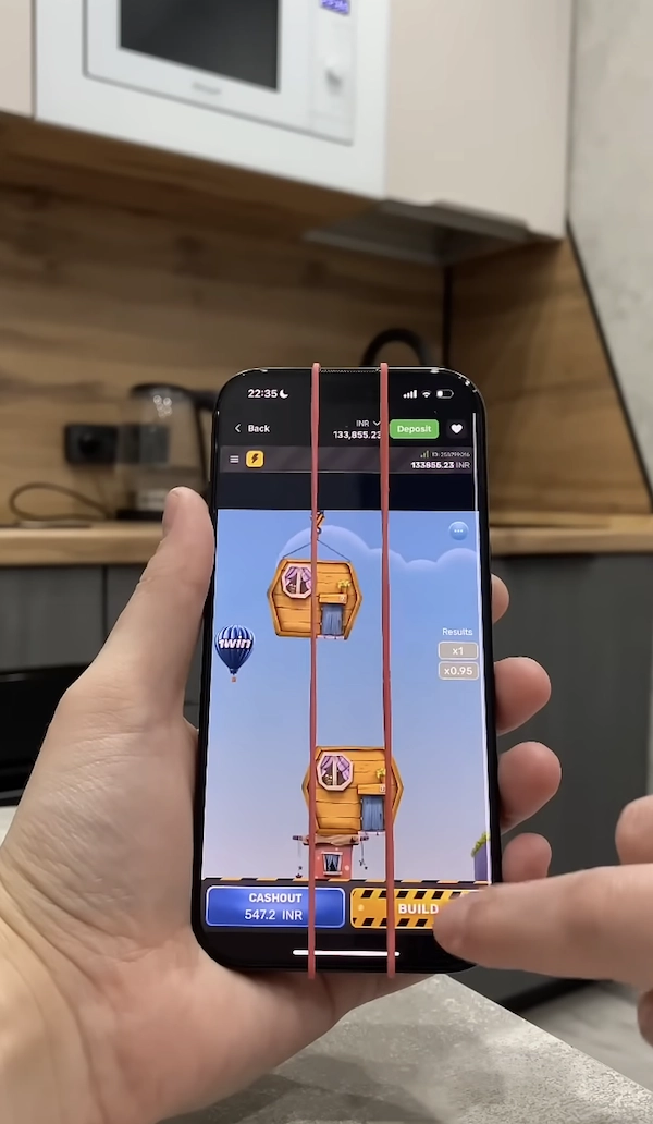 Photo d&rsquo;un smartphone tenu en main montrant le jeu de la tour casino en cours, deux &eacute;lastiques plac&eacute;s verticalement sur l&rsquo;&eacute;cran pour tenter une &ldquo;technique&rdquo;, bouton BUILD visible en bas &agrave; droite, bouton CASHOUT affichant 547.2 INR, interface de casino avec bouton Deposit vert en haut et solde affich&eacute;, d&eacute;monstration d&rsquo;une m&eacute;thode cens&eacute;e influencer le timing du jeu.